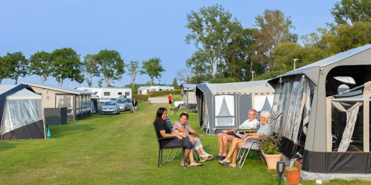 Familj njuter av en solig dag på en av Sveriges billiga campingar. Husvagnar och tält står uppradade på en grön gräsmatta.