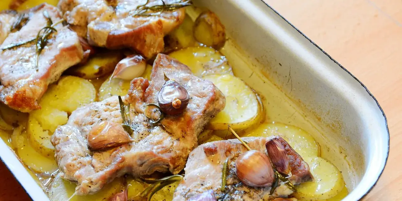 Pieczona karkówka z ziemniakami, czosnkiem i rozmarynem w naczyniu żaroodpornym.