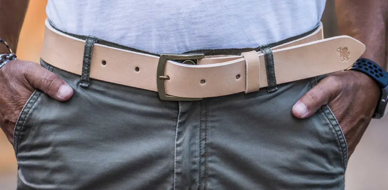 Cintura in cuoio chiaro con fibbia in ottone, indossata su pantaloni verdi. Si vede da che lato si mette la cintura.