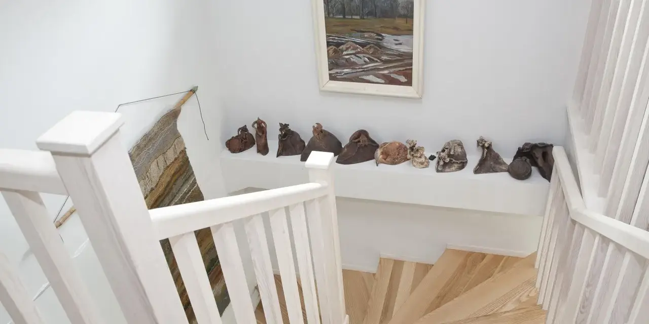 Klatka schodowa inspiracje: białe balustrady, drewniane stopnie i galeria ceramicznych rzeźb na półce.