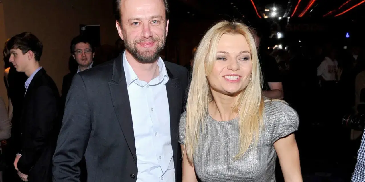 Julia Balsewicz w srebrnej sukience i mężczyzna w czarnym garniturze uśmiechają się do obiektywu.