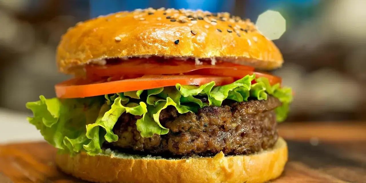 Apetyczny hamburger z sezamem, sałatą i pomidorem na desce.