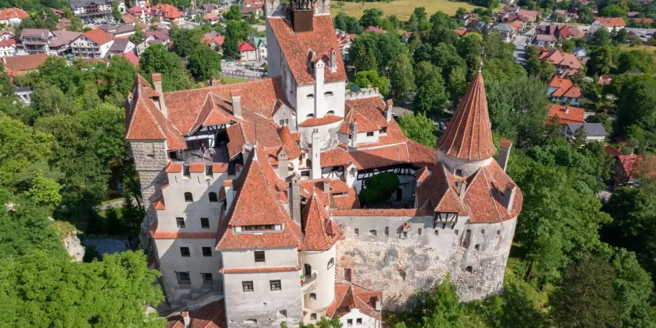 Dracula zamek, majestatyczna twierdza z czerwonymi dachami, otoczona zielenią i malowniczą wioską.