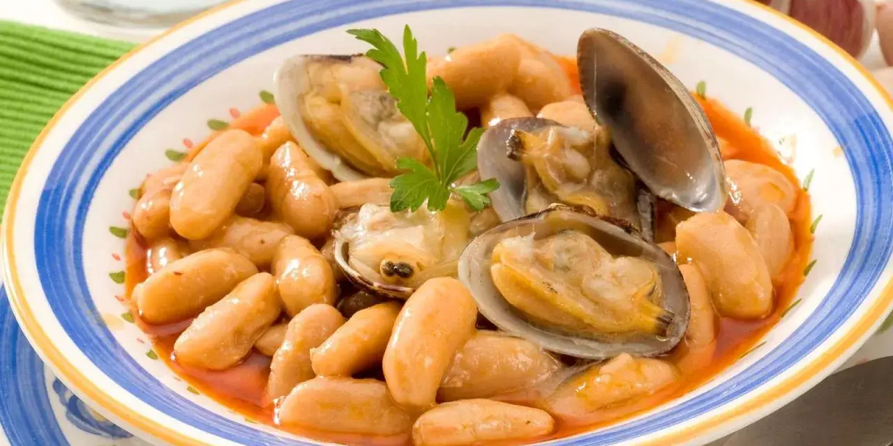 Plato de fabes con almejas, un guiso tradicional asturiano con judías blancas tiernas y jugosas almejas, decorado con perejil fresco.