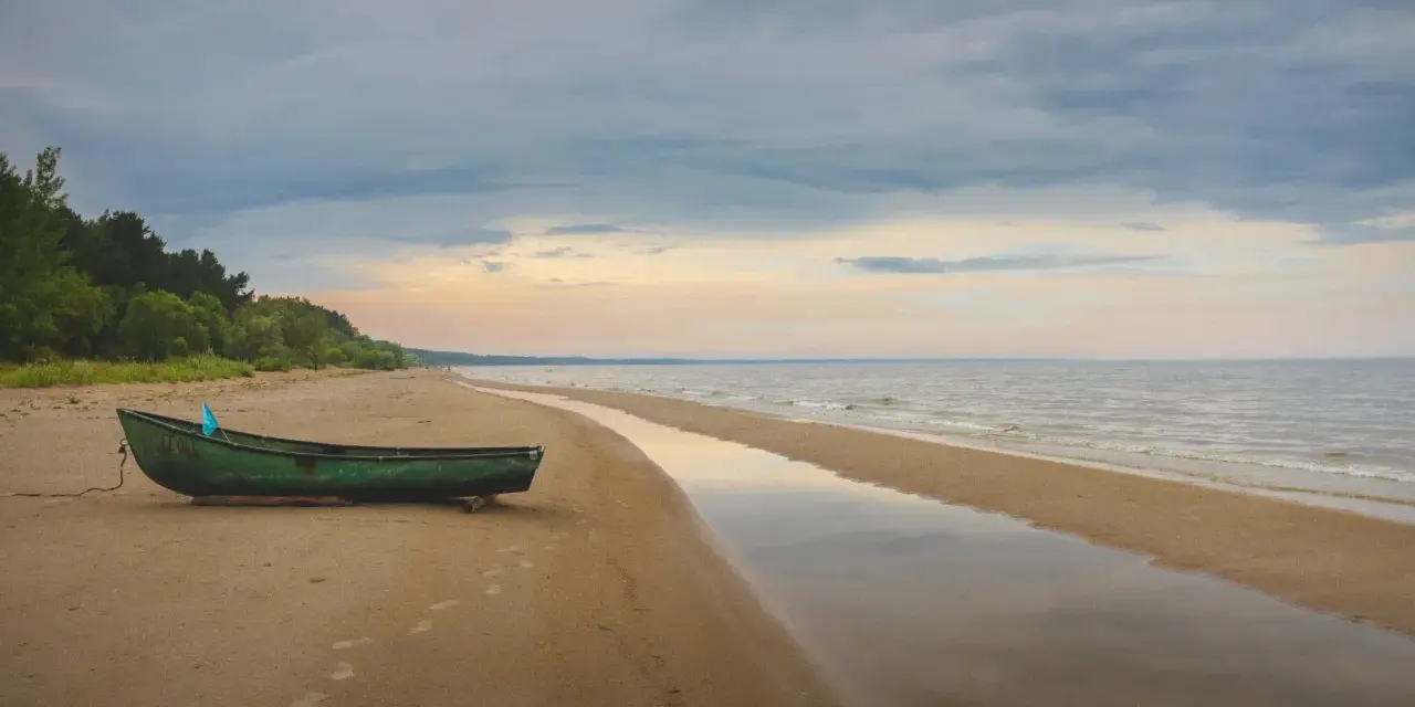 Zielona łódź na piaszczystej plaży Mierzei Wiślanej, idealne miejsce na camping. Woda odbija niebo, tworząc spokojny krajobraz.