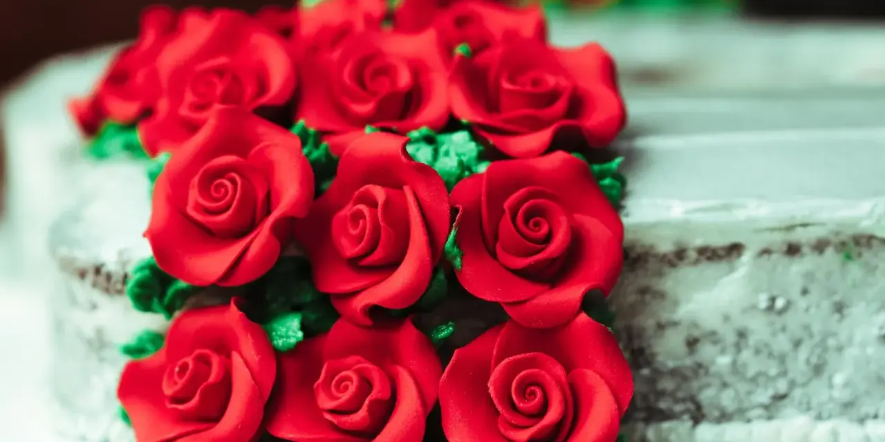 Un mazzo di rose rosse in pasta di zucchero adorna una torta.