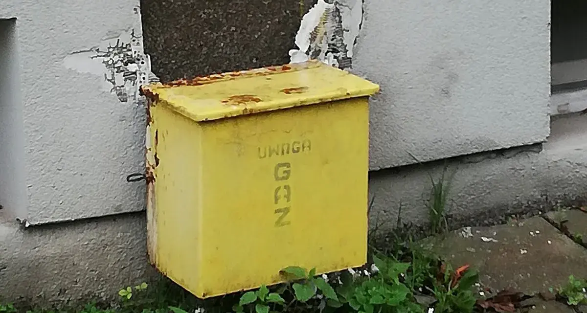 Żółta skrzynka gazowa w elewacji budynku, z napisem "UWAGA GAZ".