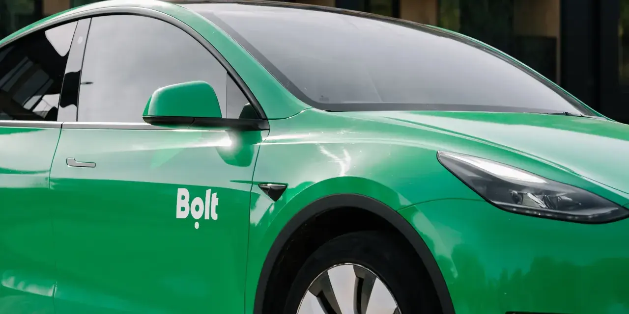 Zielone auto z oklejeniem Bolt. Widoczna część drzwi, lusterko i fragment maski.