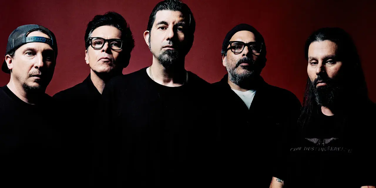 Pięciu mężczyzn, zespół Deftones Polska, pozuje do zdjęcia na ciemnoczerwonym tle.