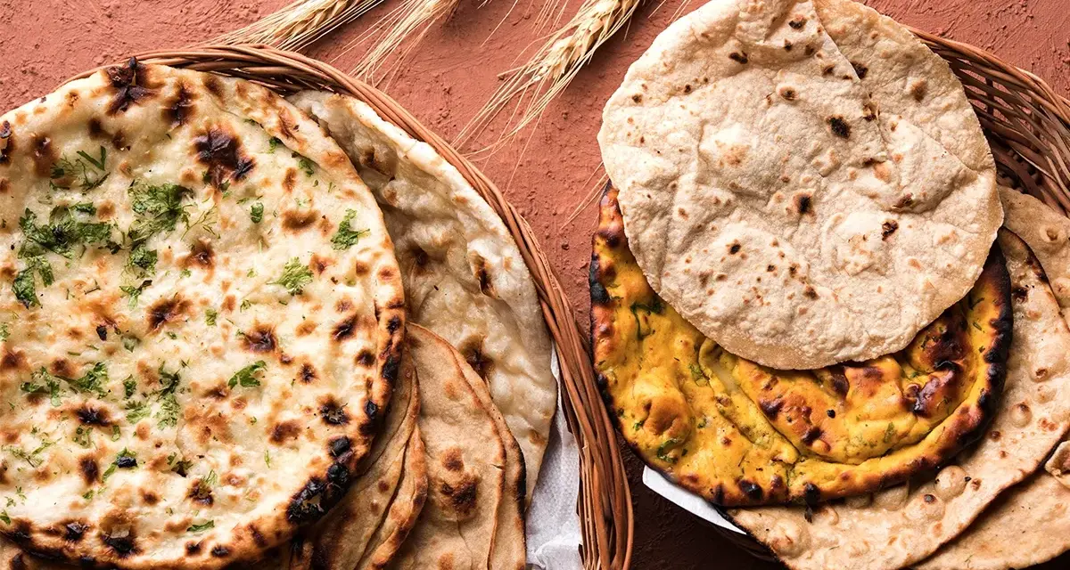Dwa koszyki pełne pysznego chleba indyjskiego, w tym aromatyczny naan z kolendrą i klasyczny roti, ozdobione kłosami zboża.