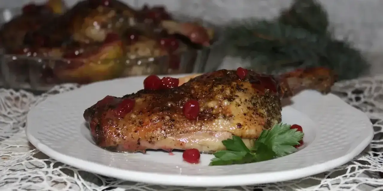 Pyszne, pieczone udka z kaczki z żurawiną i ziołami, podane na białym talerzu.