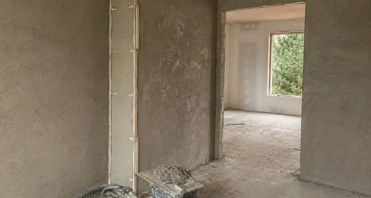 Ściany pokryte surowym tynkiem wapienno cementowym, gotowe do dalszych prac. Widać wiadro z zaprawą i narzędzia.