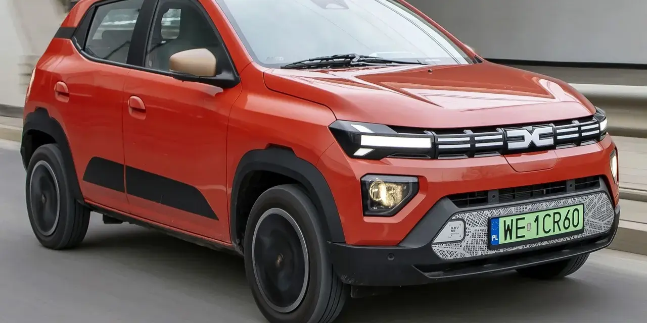 Pomarańczowy Dacia Spring, najtańsze auto elektryczne, jedzie po drodze.