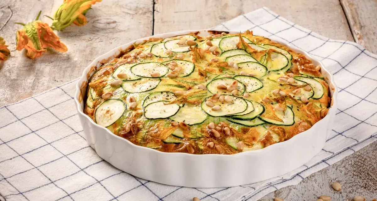 Frittata di zucchine al forno, guarnita con pinoli e fiori di zucca, pronta per essere gustata.