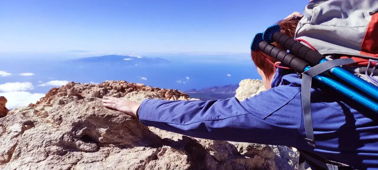 Blick vom Gipfel nach der Teide Wanderung. Ein Wanderer lehnt sich auf Felsen, mit Blick auf das weite Meer und ferne Inseln.