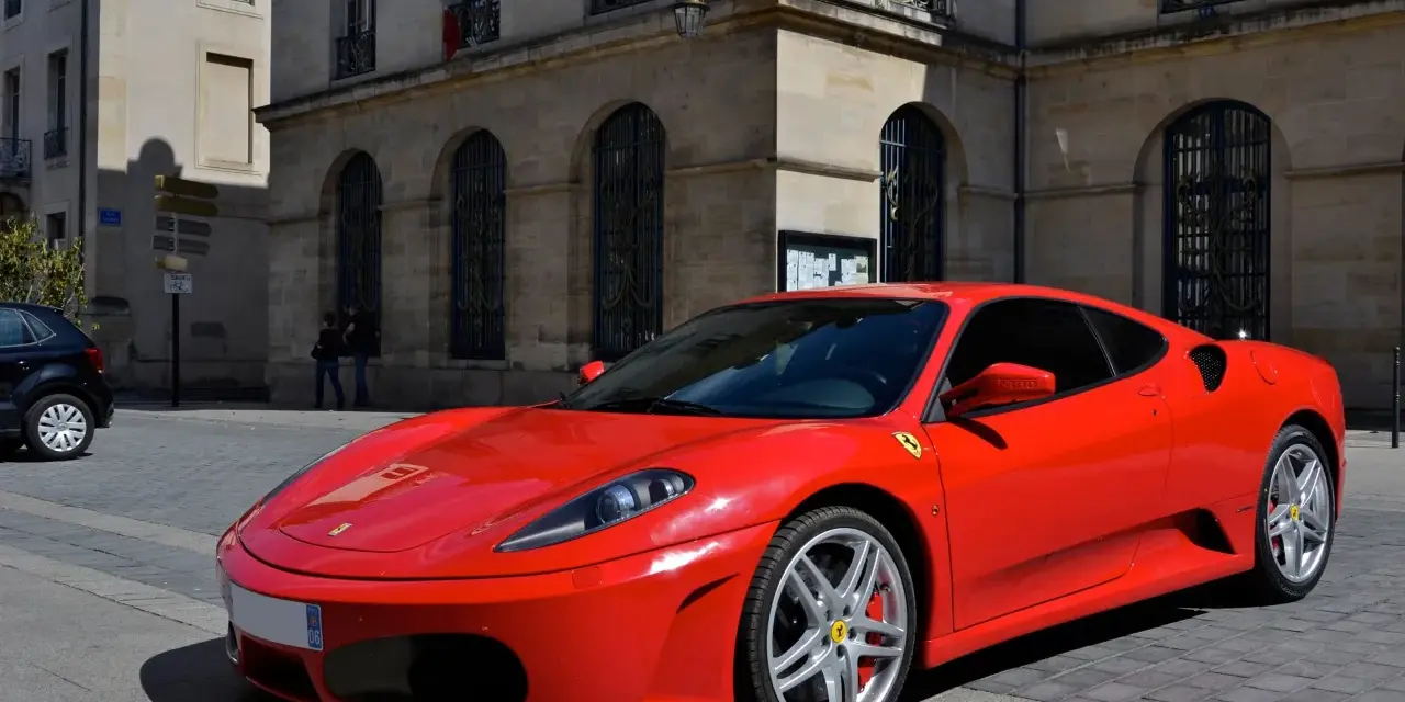 Czerwone Ferrari F430 zaparkowane na brukowanej ulicy przed kamienną kamienicą.
