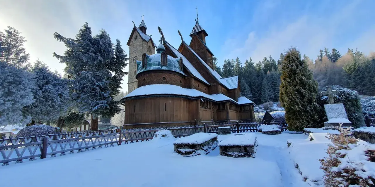 Drewniana świątynia Wang w Karkonoszach, otoczona ośnieżonymi drzewami i cmentarzem, wygląda magicznie w zimowym słońcu.