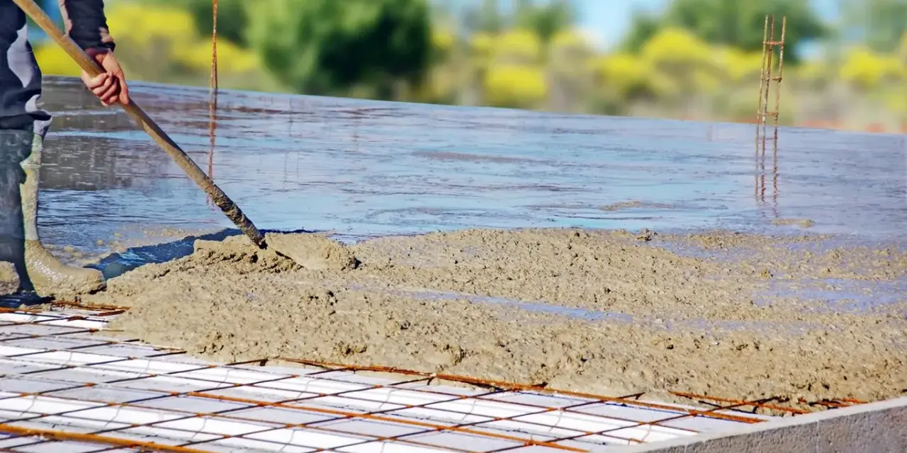 Coulée de béton frais sur une armature métallique pour assurer l'épaisseur dalle maison. Le travailleur étale le béton avec une pelle.