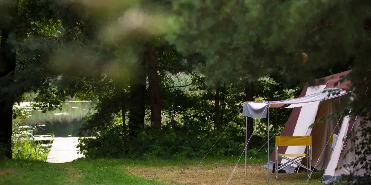 Namiot i krzesło na tle jeziora i lasu. Idealne pola namiotowe Mazury dla miłośników natury.