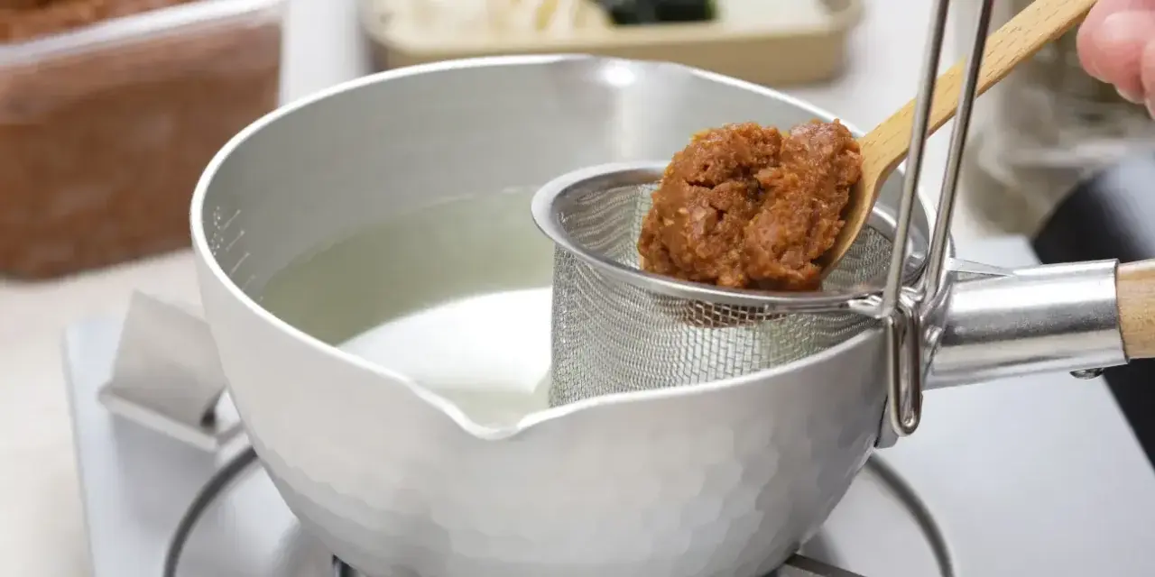 Łyżka z pastą miso trafia do bulionu. Tak przygotowuje się bazę do zupy, pytasz miso co to? To fermentowana pasta sojowa.