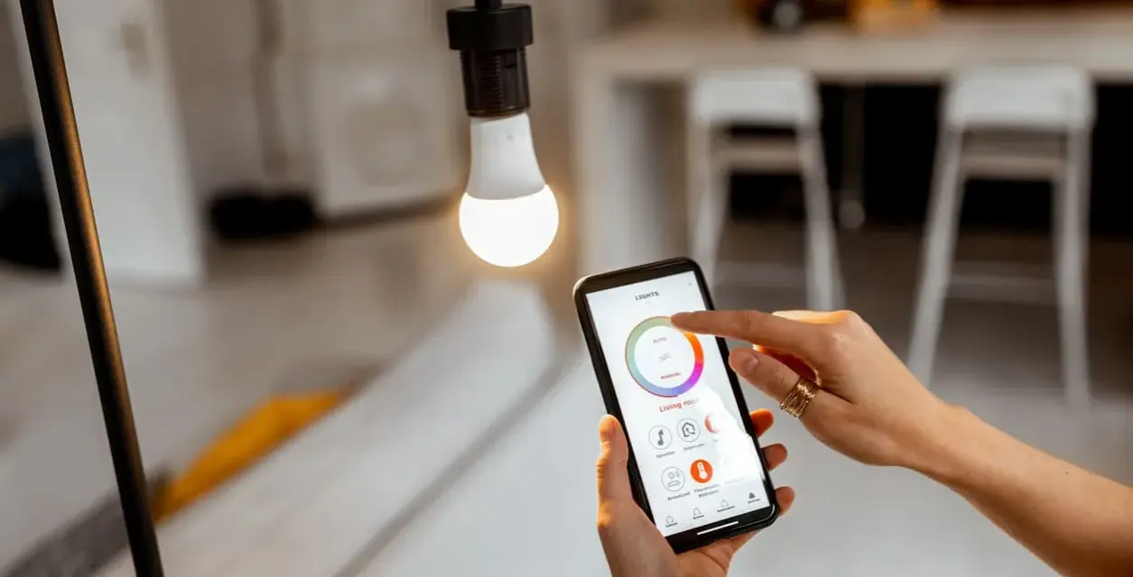 Mano ajustando el control de iluminacion domotica en un smartphone para regular la luz de una bombilla.