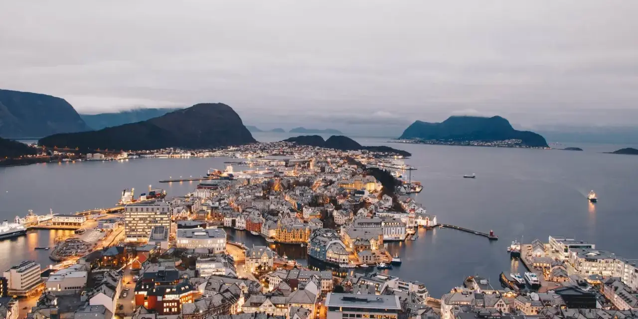 Vacker stad vid vattnet i Norge, med upplysta hus och berg i bakgrunden. En dröm att bila i Norge.