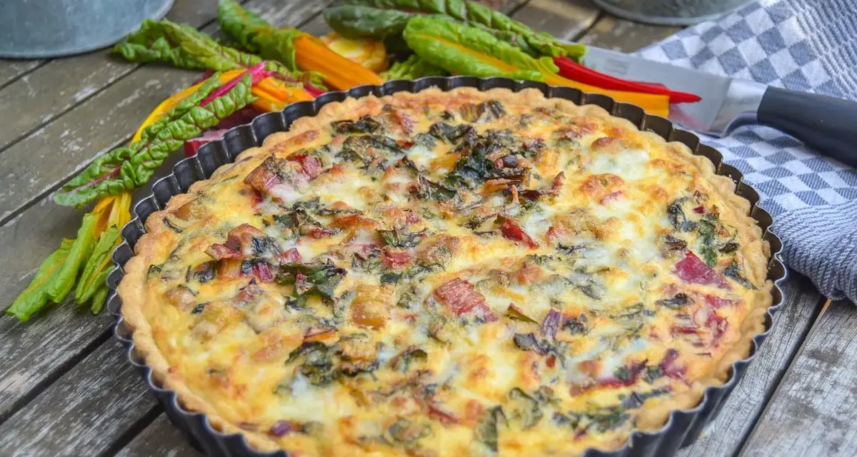 Herzhaftes Mangold Quiche Rezept, frisch gebacken und bereit zum Genießen. Bunte Mangoldstiele liegen daneben.