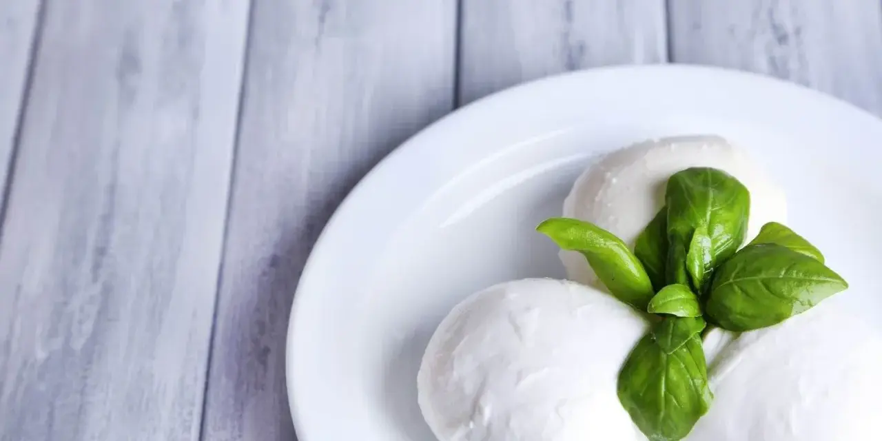 Trzy kulki serka mozzarella z listkami bazylii na białym talerzu. Idealne do sałatki, znasz ser mozzarella kcal?