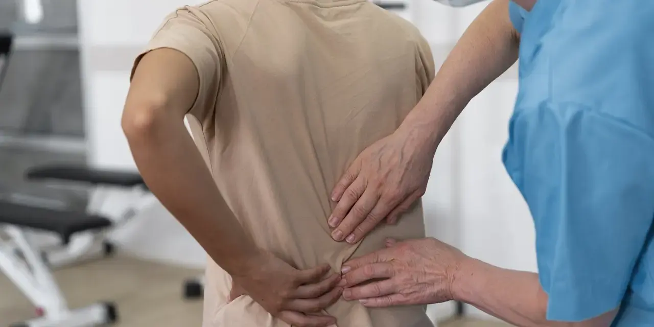 Fizjoterapeuta bada plecy pacjentki, która odczuwa ból po upadku na plecy. Konsekwencje urazu są widoczne.