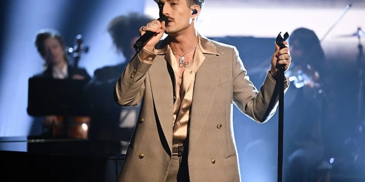 Un cantante con un completo gessato e camicia satinata, microfono in mano, incarna il **dandy significato** con stile sul palco.