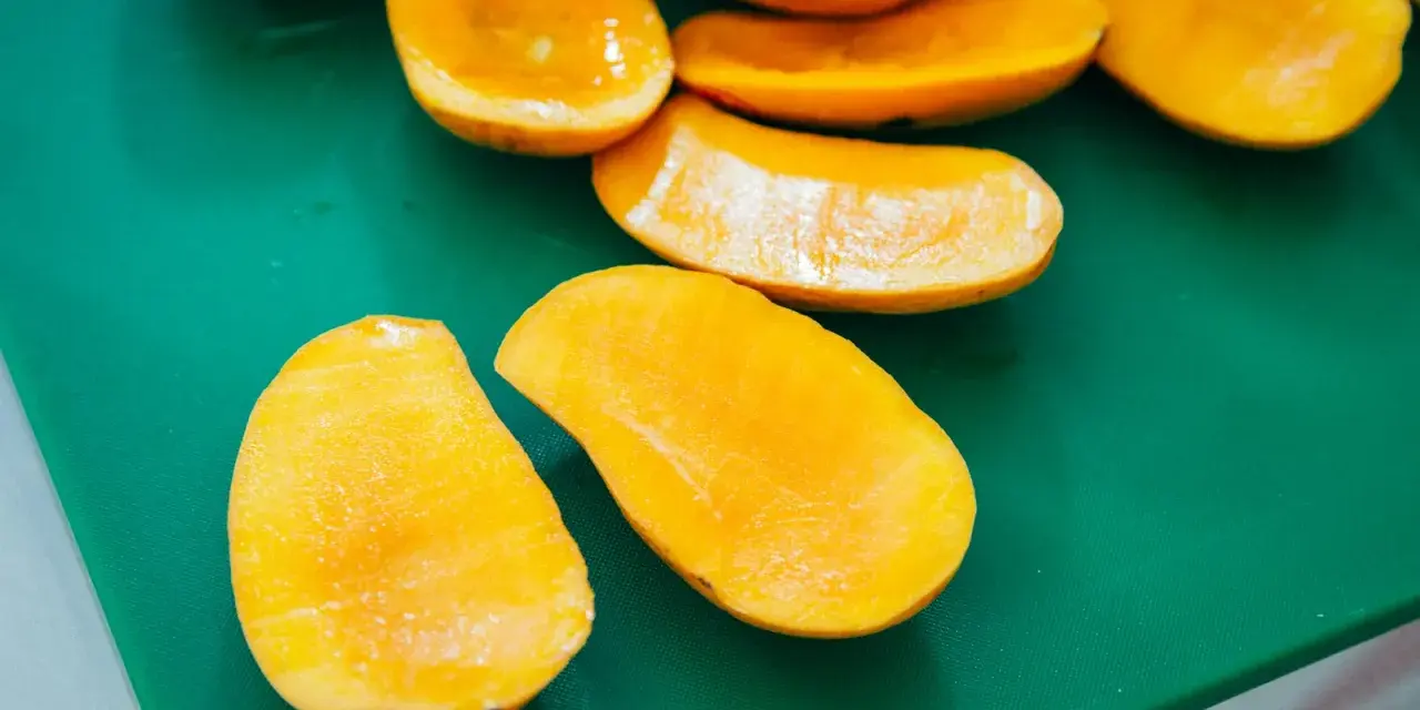 Pokrojone w łódeczki, soczyste mango w intensywnym kolorze, jakby w ciąży z owocową obfitością, leżą na zielonej desce.