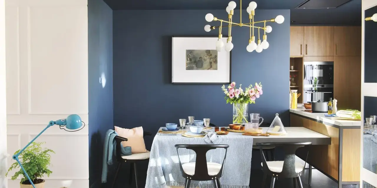 El azul oscuro combina con tonos pastel, madera y dorado. Un comedor elegante con mesa, sillas negras, lámpara dorada y flores.