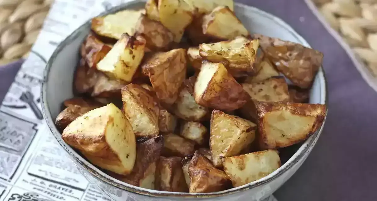 Patate dorate e croccanti in friggitrice ad aria, servite in una ciotola su carta di giornale.