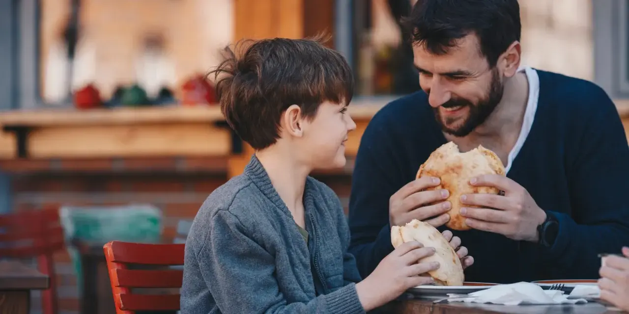 Vater und Sohn teilen sich ein Brot. Vielleicht plant der Vater ein Wechselmodell, um Unterhalt zu sparen, aber im Moment genießen sie die gemeinsame Zeit.