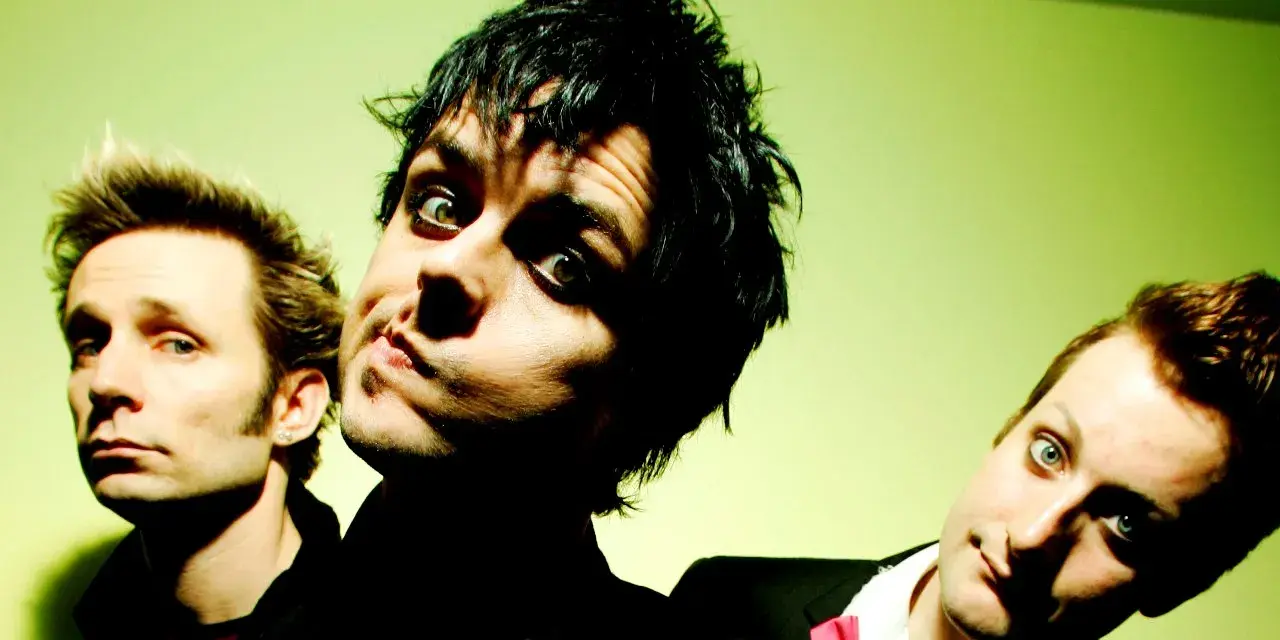 Trzej członkowie Green Day: Billie Joe Armstrong, Mike Dirnt i Tré Cool, pozują do zdjęcia na zielonym tle.