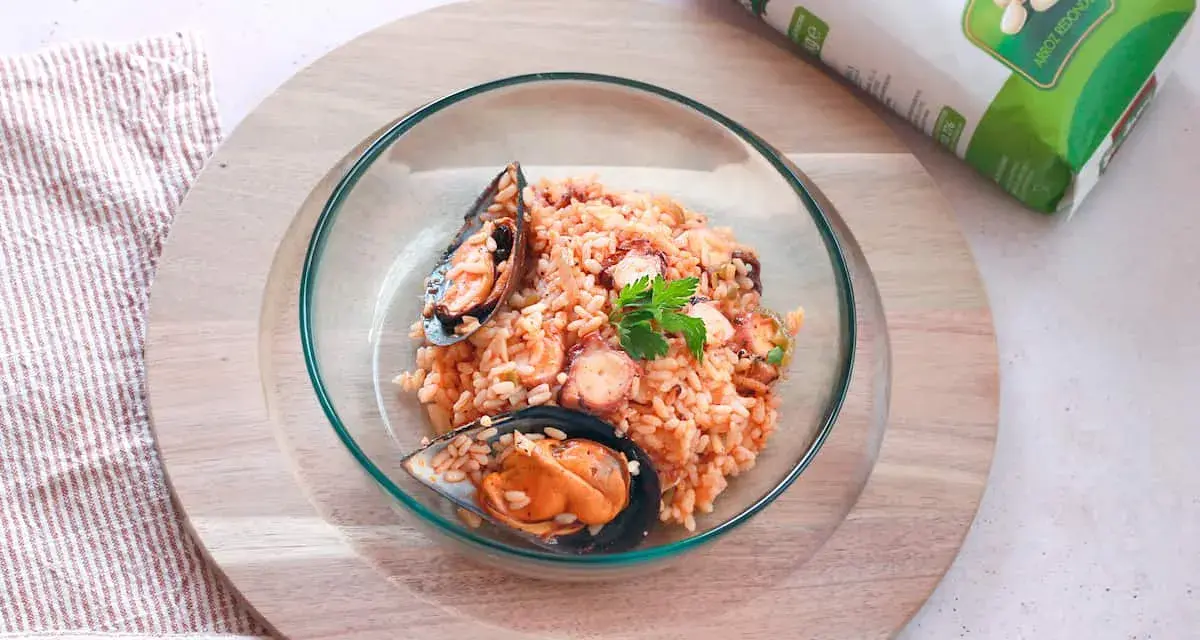 Delicioso arroz con pulpo y mejillones, servido en un cuenco de cristal sobre una tabla de madera.