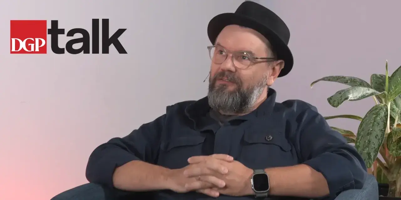 Mężczyzna w okularach i kapeluszu siedzi, rozmawiając. Obok logo DGP talk.