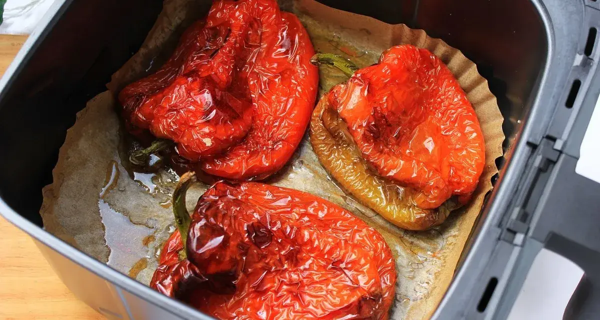 Tres pimientos rojos asados en freidora de aire, con la piel arrugada y jugosos, listos para disfrutar.