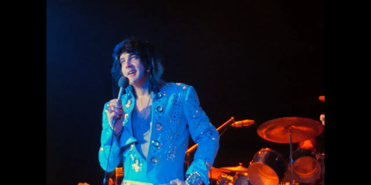 Elvis Presley, in einem glitzernden blauen Anzug, singt ins Mikrofon. Ein Bild, das an seine legendären Elvis Presley Filme erinnert.