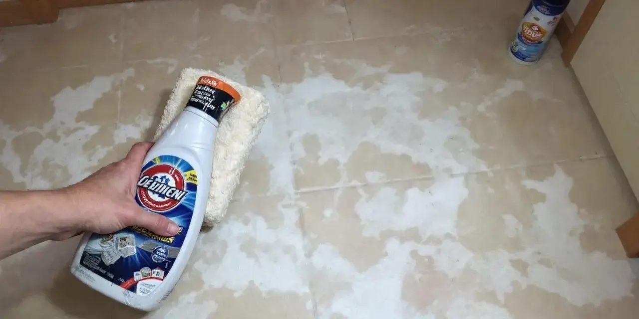Main tenant tente de nettoyer un voile de ciment qui ne part pas sur le carrelage avec un produit.