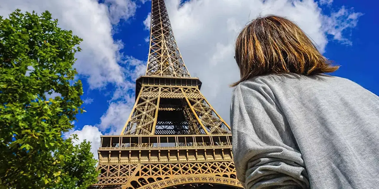 Persona admira la imponente Torre Eiffel bajo un cielo azul con nubes.