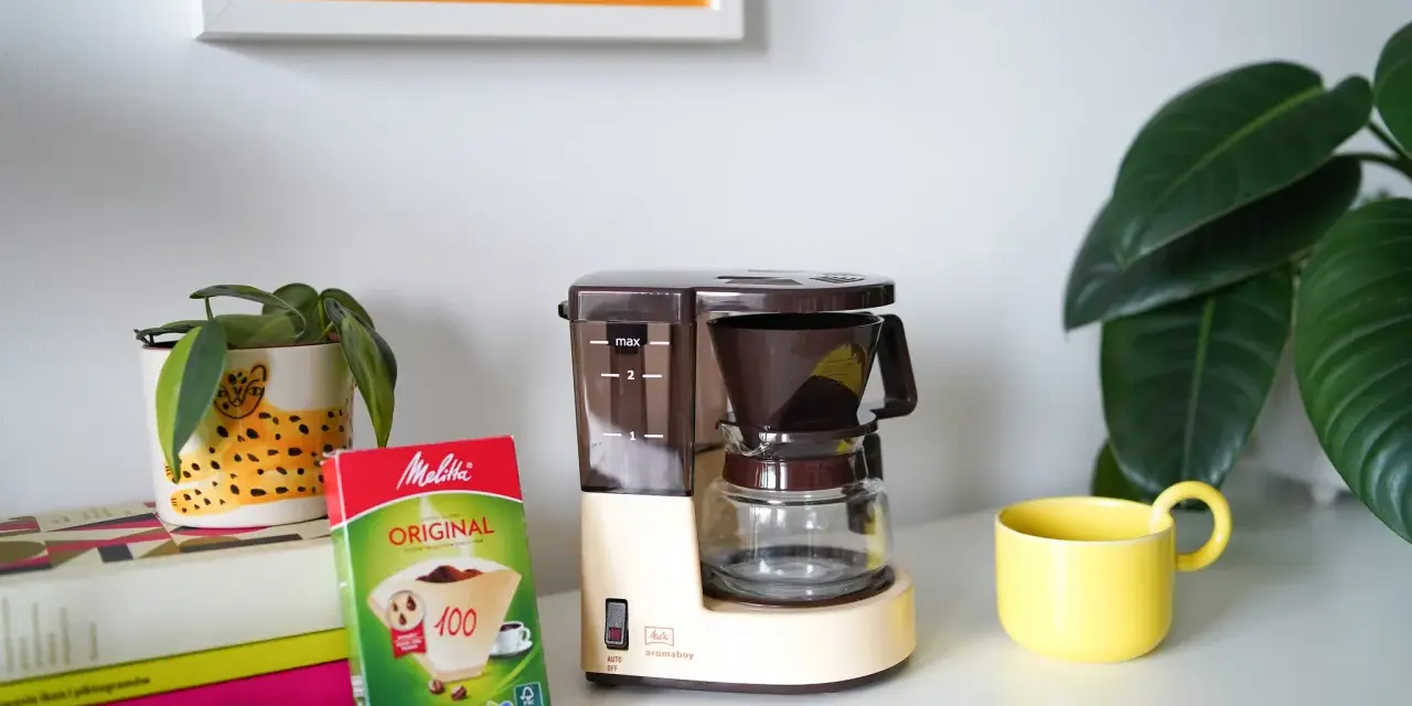 Kawiarka przelewowa Melitta Aromaboy gotowa do zaparzenia porannej kawy. Obok filtry i żółta filiżanka.