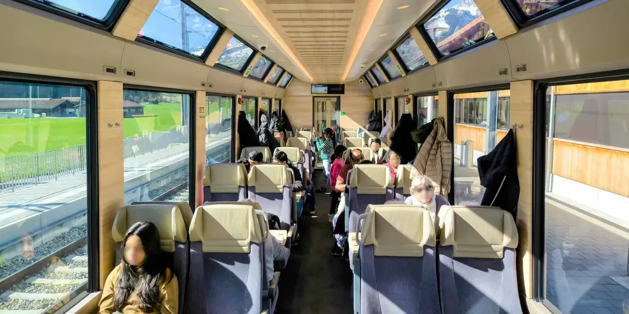 Passengers enjoy the scenic views from the panoramic windows of a train on the Golden Pass Line, with mountains visible outside.