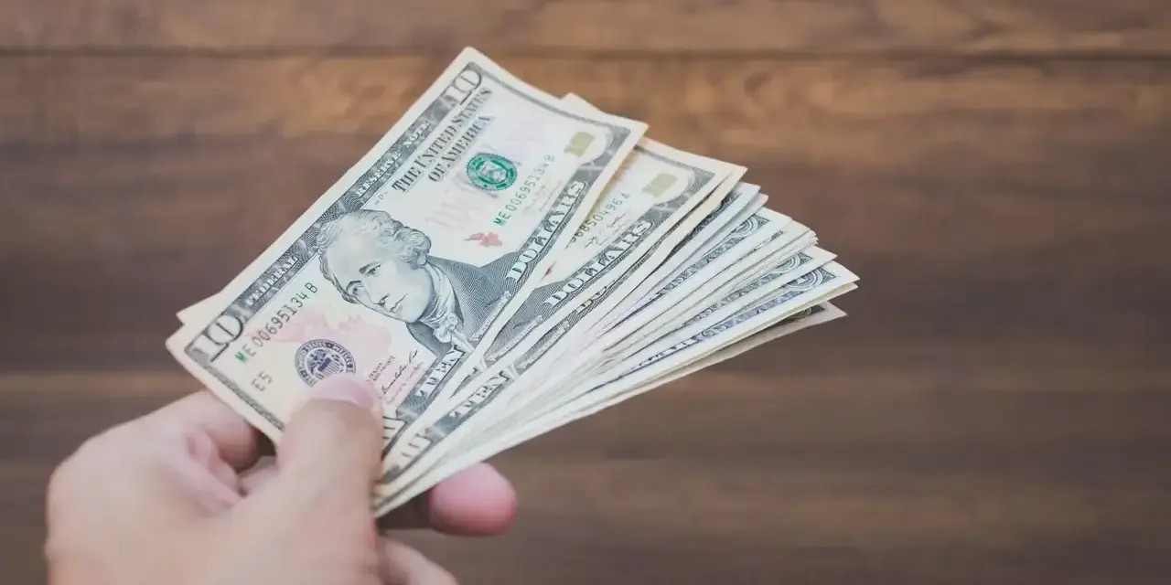 Dłoń trzyma plik banknotów dziesięciodolarowych. To może być zapłata za trzynastkę lub po prostu nagroda.