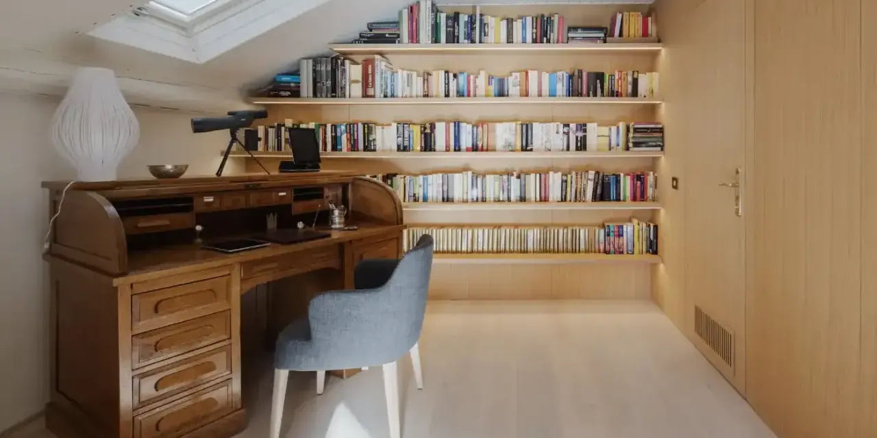 Scrivania in legno massiccio e libreria moderna illuminata, un perfetto esempio di come abbinare e mischiare arredamento classico e moderno in uno studio mansardato.