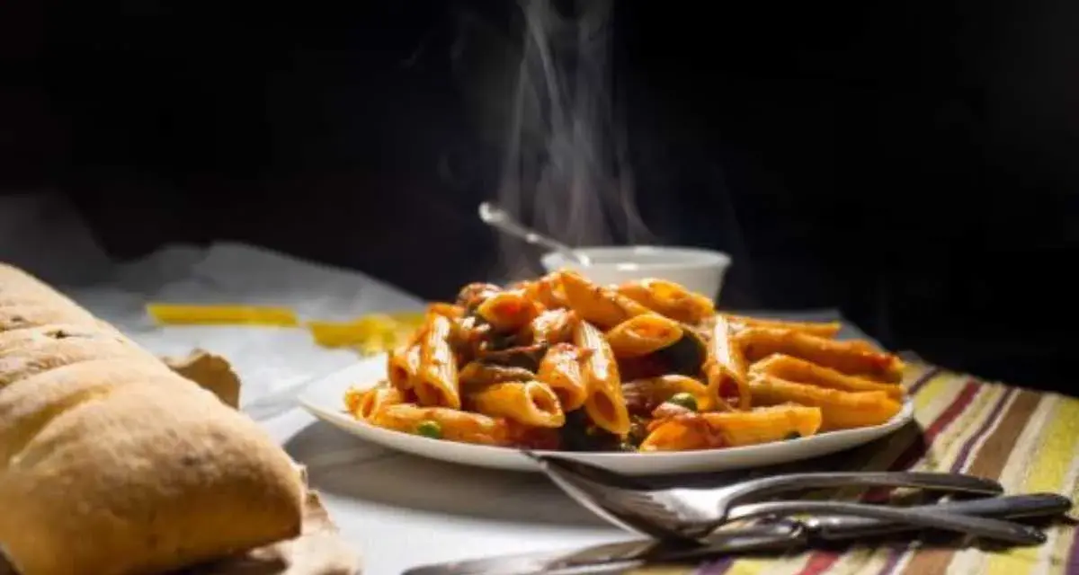 Piatto fumante di penne alla vodka, con pane croccante e posate. Un classico confortante.