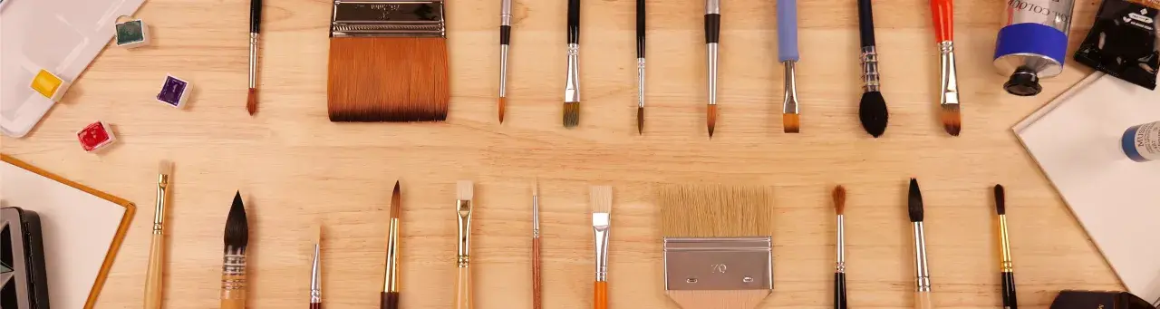 Collection de différents types de pinceaux peinture, ronds et plats, aux poils variés, disposés sur un fond en bois.