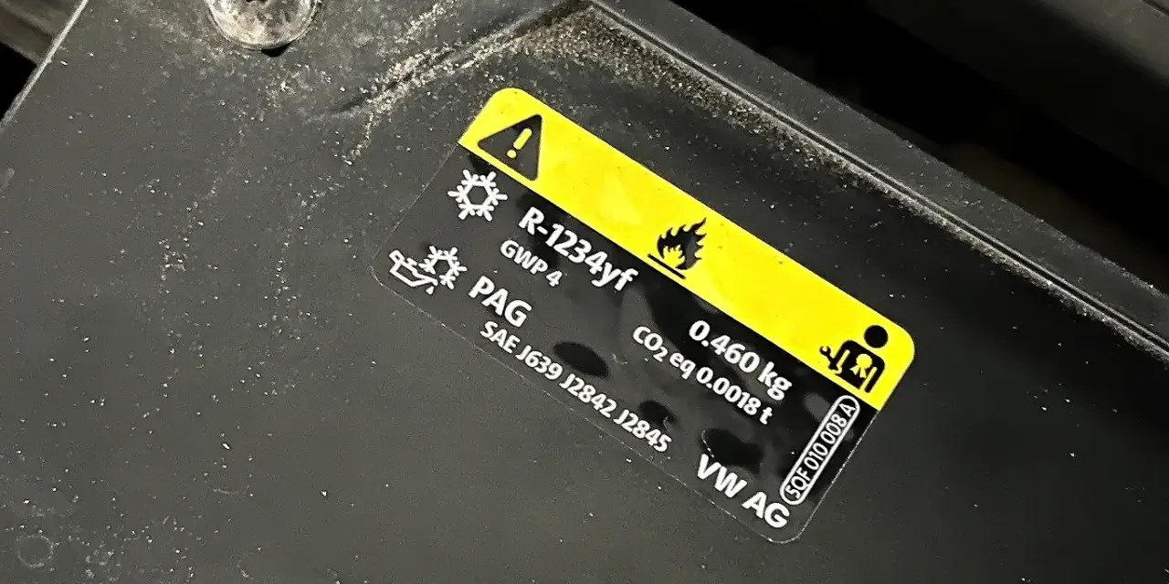Naklejka informuje o ilości czynnika klimatyzacji R-1234yf (0.460 kg) i typie oleju PAG w samochodzie VW AG.