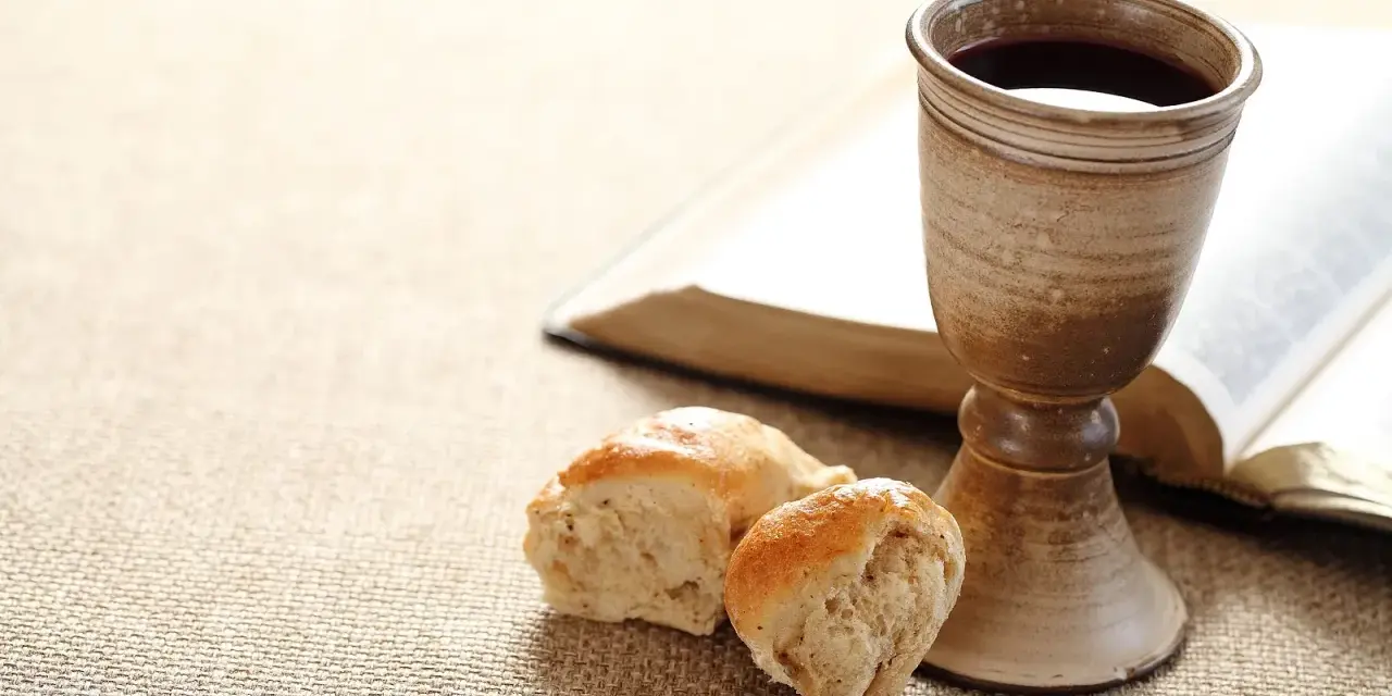 Kelch mit Rotwein, Brot und aufgeschlagenes Buch. Symbol für das christliche Abendmahl und dessen Bedeutung im Glauben.