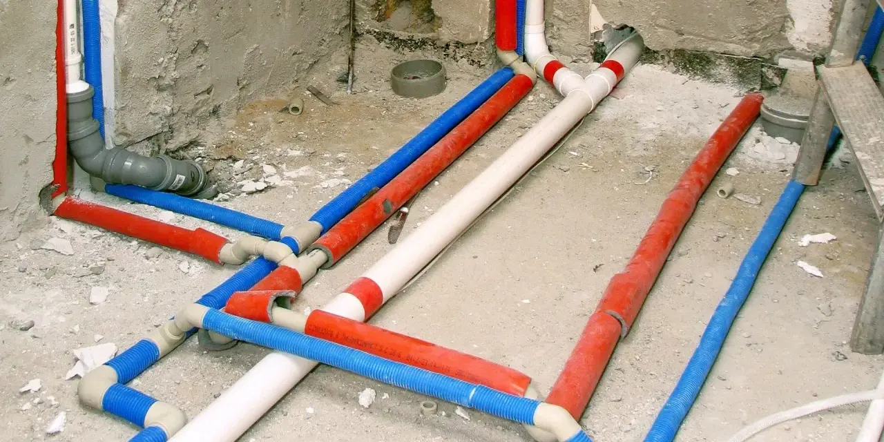 Skomplikowana instalacja wodna z rurami w kolorach czerwonym, niebieskim i białym, przygotowana do ukrycia pod tynkiem.